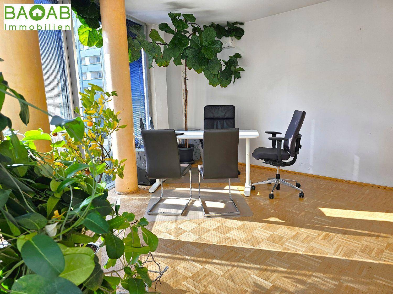 Moderner Büroraum mit Holzboden, großen Pflanzen und einem Schreibtisch für zwei Personen.