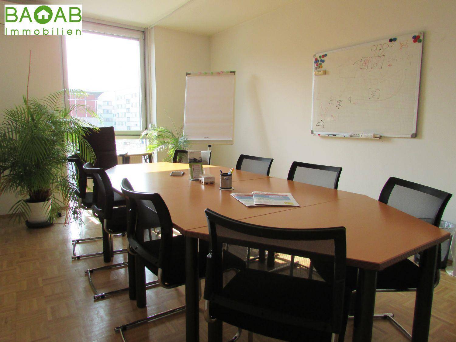 Konferenzraum mit großem ovalen Tisch, mehreren Stühlen und Whiteboard, ideal für Besprechungen.