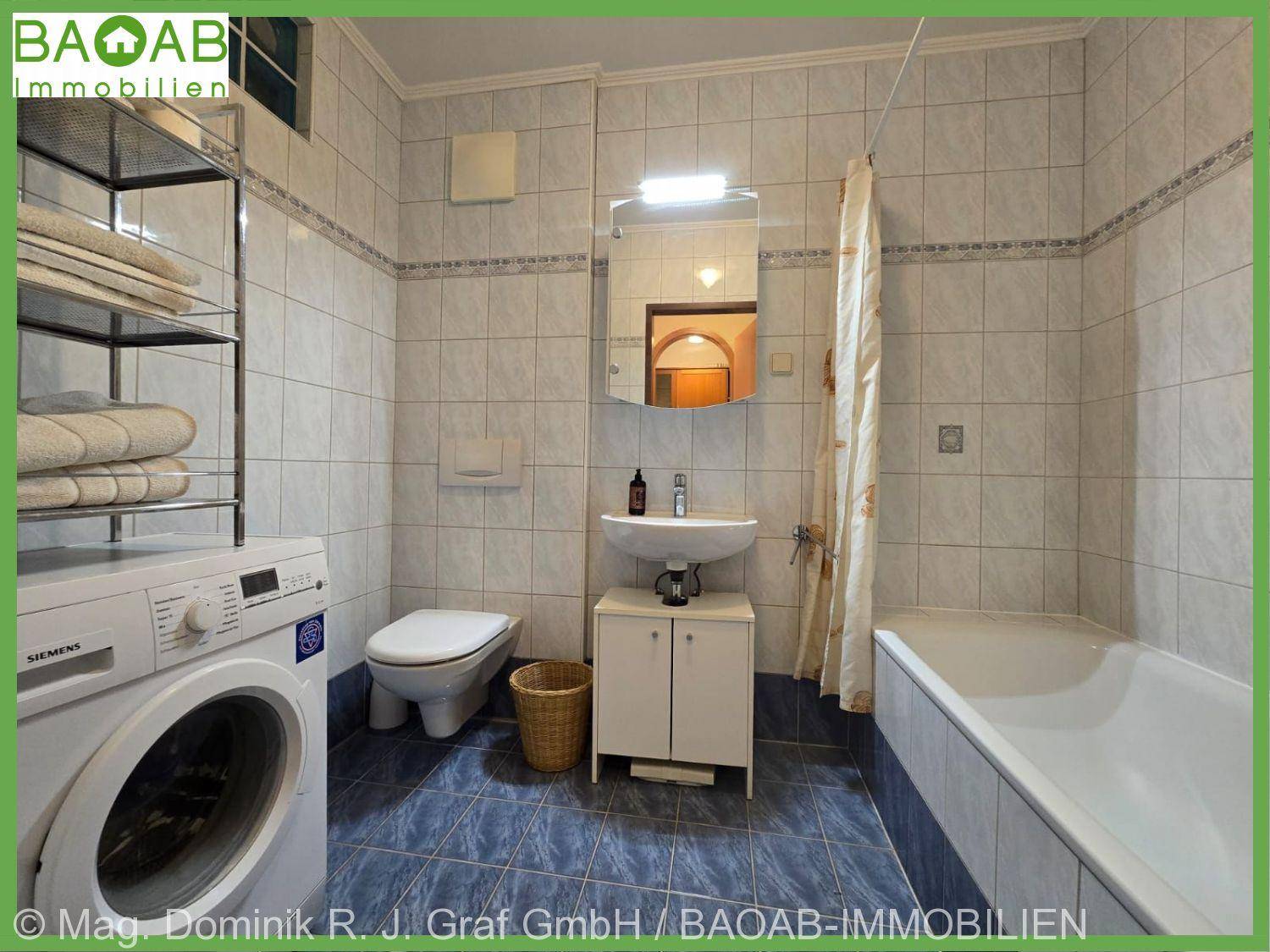 Gefliestes Badezimmer mit Badewanne, WC und Waschmaschine in hellen Farben.