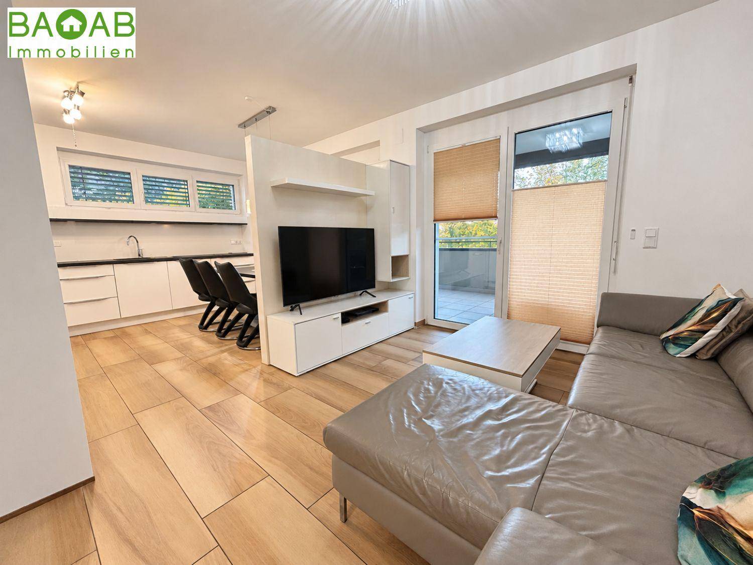 Offener Wohnbereich mit Sofa, Fernseher und angrenzender Küche, mit Zugang zu einem Außenbereich.