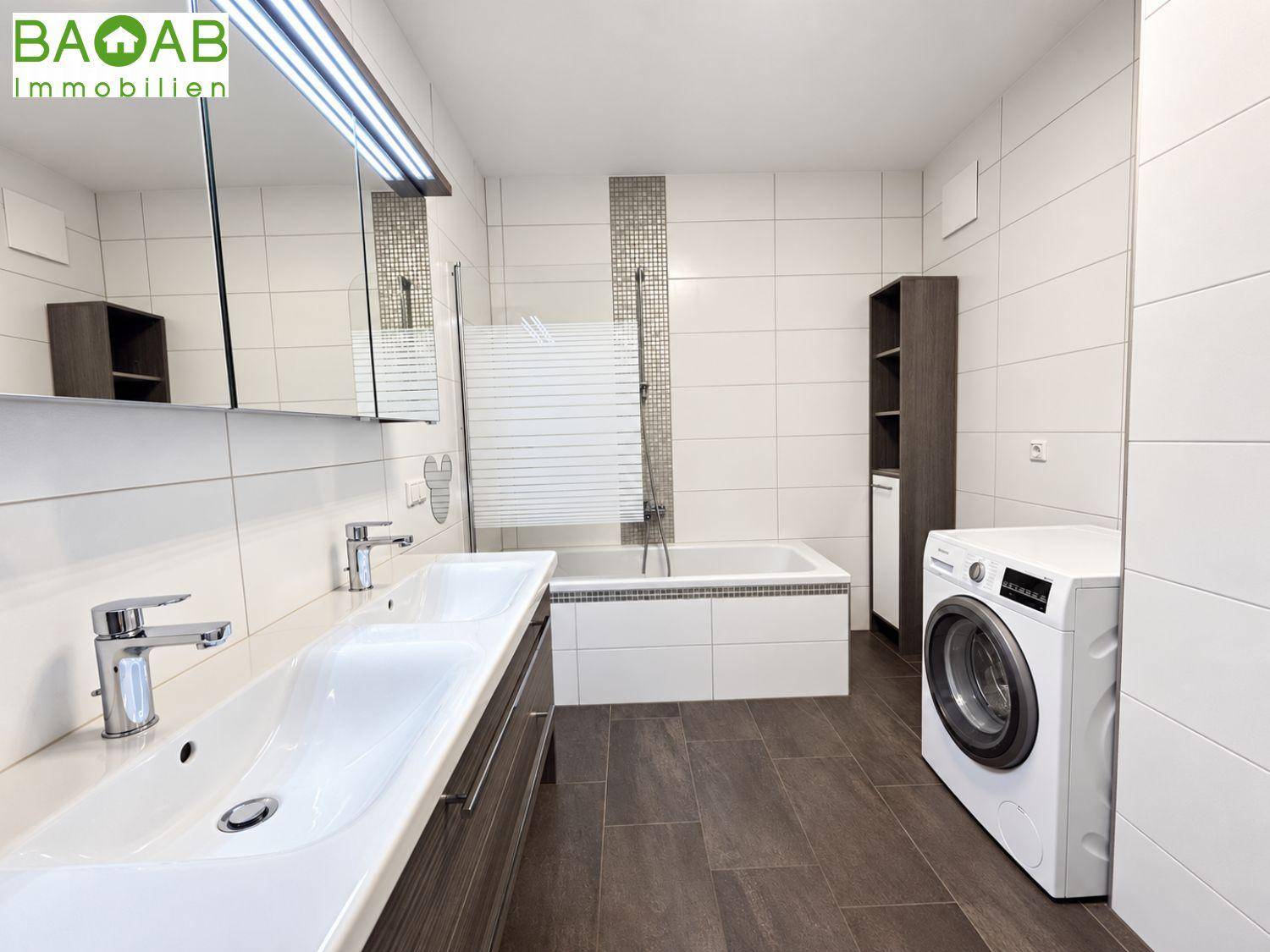 Modernes Badezimmer mit Doppelwaschbecken, Badewanne mit Duschfunktion und einer Waschmaschine.