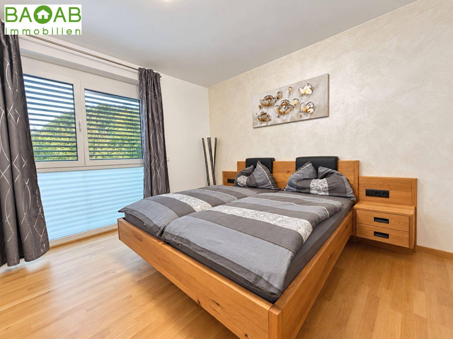 Helles Schlafzimmer mit einem Holzbett, Parkettboden und einem großen Fenster mit Blick ins Grüne.