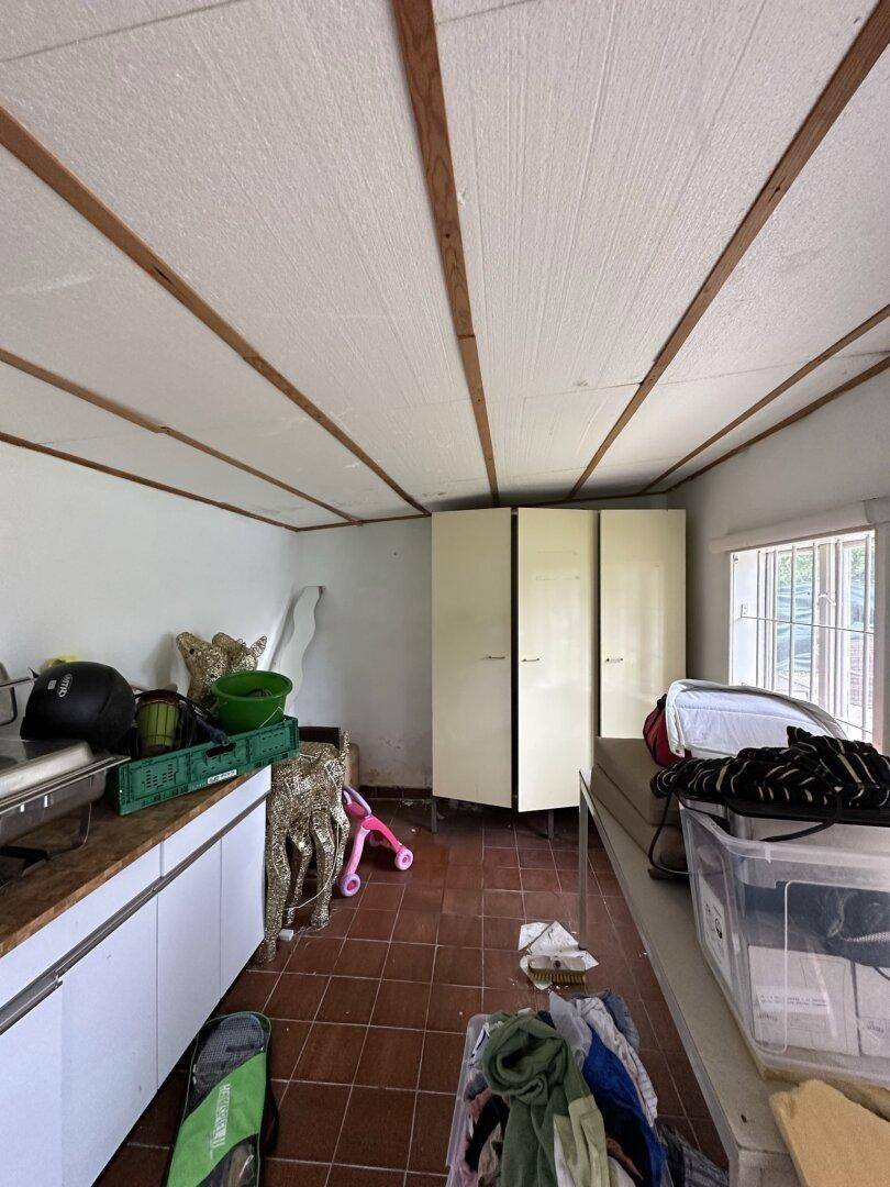 Unaufgeräumter Abstellraum mit gefliestem Boden, Holzdeckenbalken und einem Fenster.