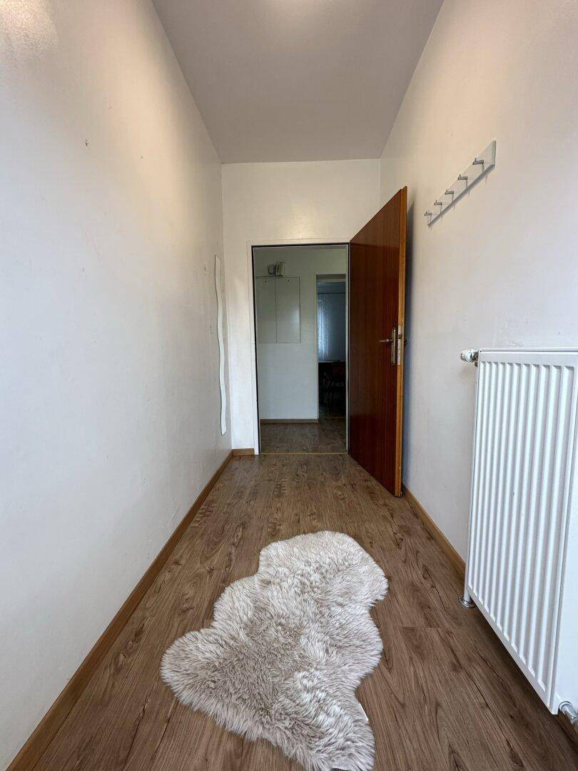 Heller Flur mit Holzboden, weiß gestrichenen Wänden und Garderobenhaken.