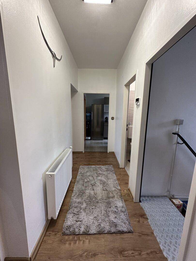 Langer Flur mit Holzboden, weiß gestrichenen Wänden und Zugang zu weiteren Räumen.