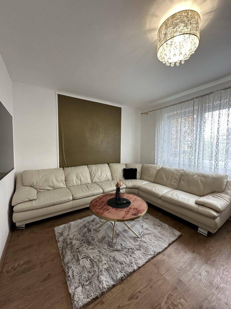 Geräumiges Wohnzimmer mit großem Ecksofa, Holzboden und Fenster mit Vorhängen.