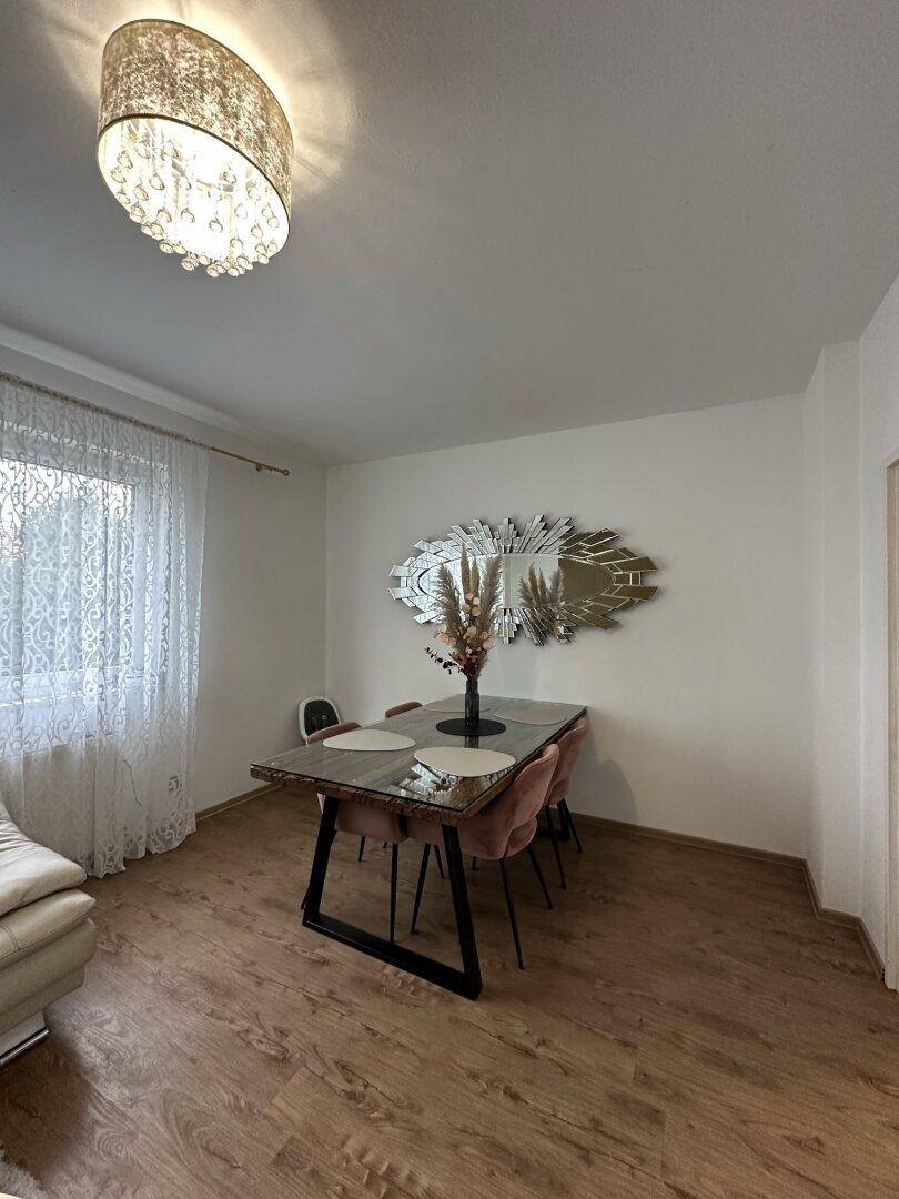 Essbereich mit modernem Esstisch, rosa Stühlen und dekorativem Wandspiegel.