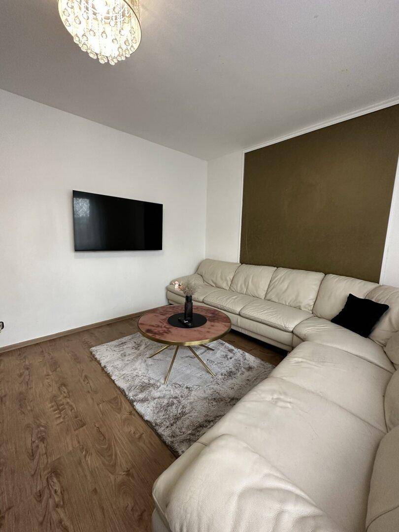 Gemütliches Wohnzimmer mit beigem Ecksofa, Holzboden und modernem Couchtisch.