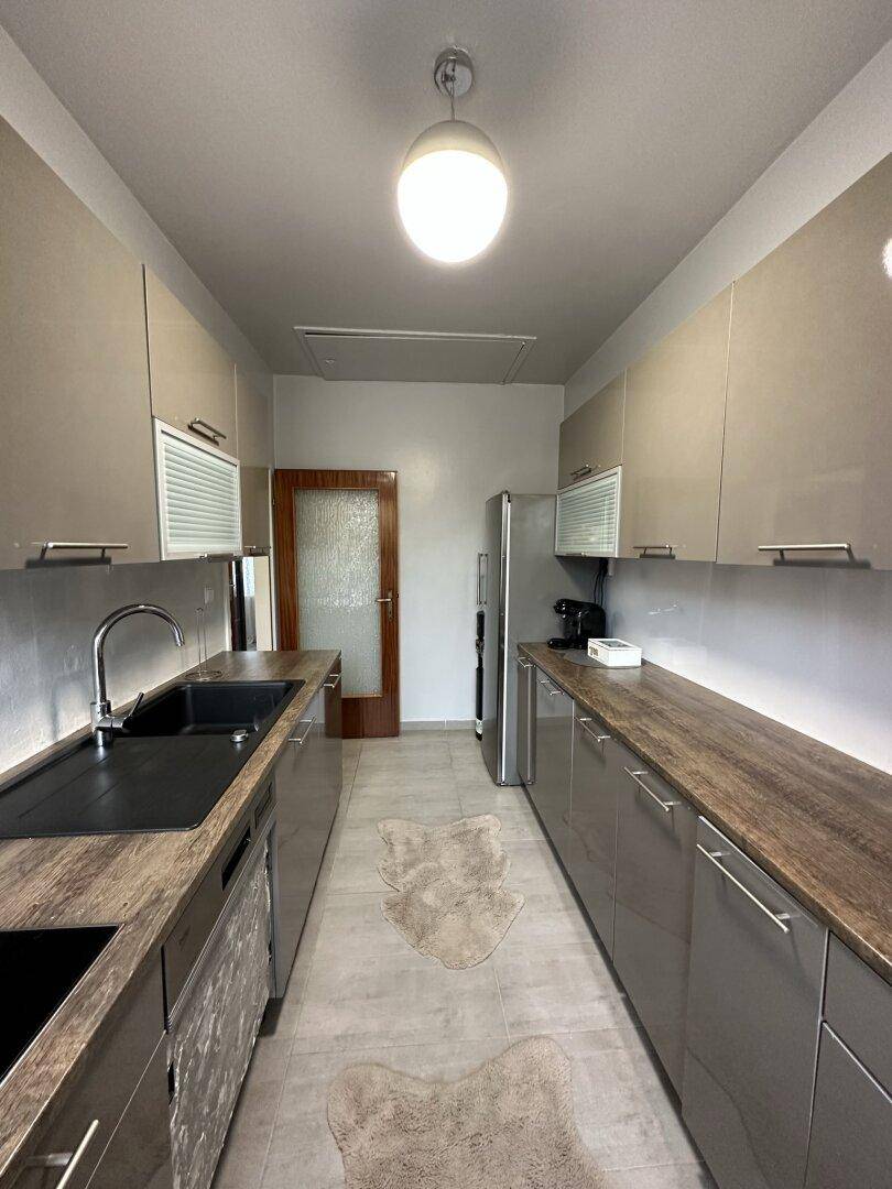 Moderne, schmale Küche mit beigefarbenen Hochglanzschränken, Holzarbeitsplatten und integrierten Geräten.