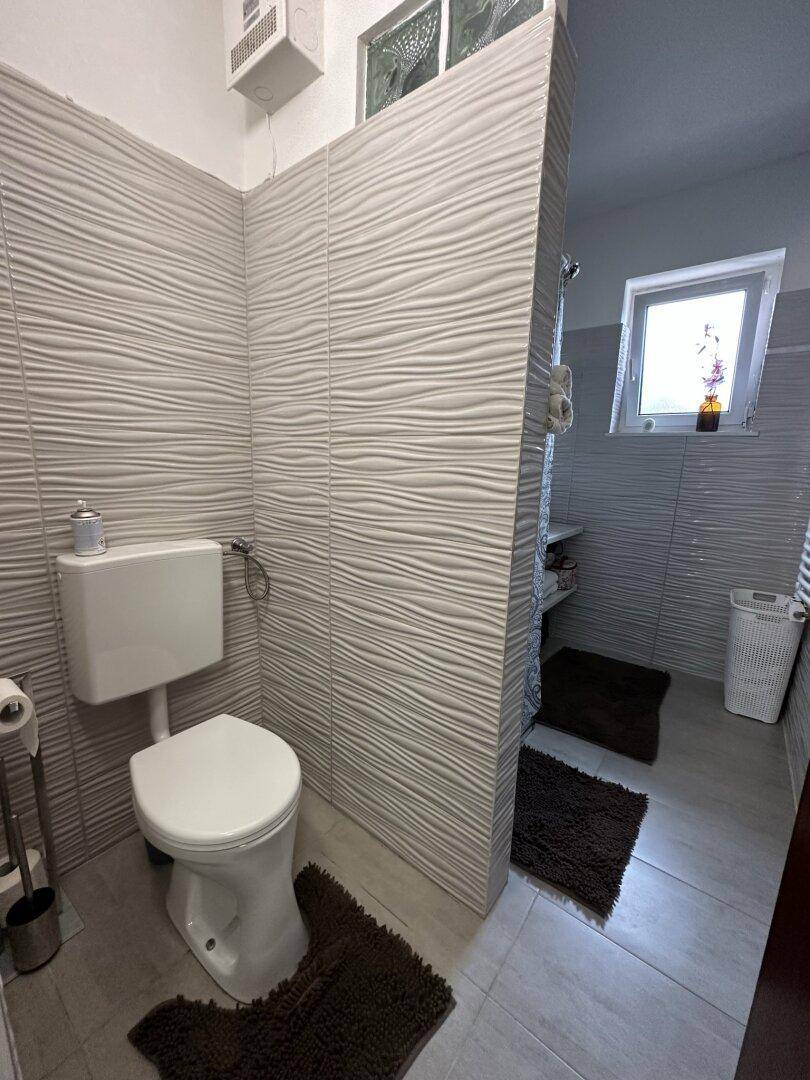 Modernes Badezimmer mit strukturierten grauen Fliesen, Toilette und Duschbereich.