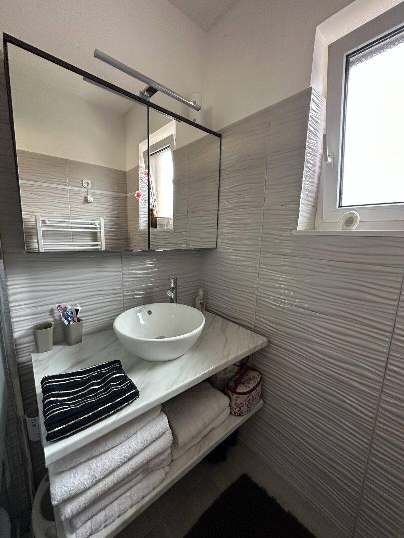 Badezimmer mit modernem Waschbecken, Spiegelschrank und Fenster für Tageslicht.