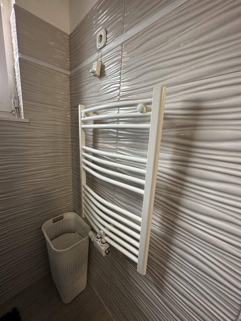 Badezimmer mit beheiztem Handtuchhalter und strukturierten grauen Wandfliesen.