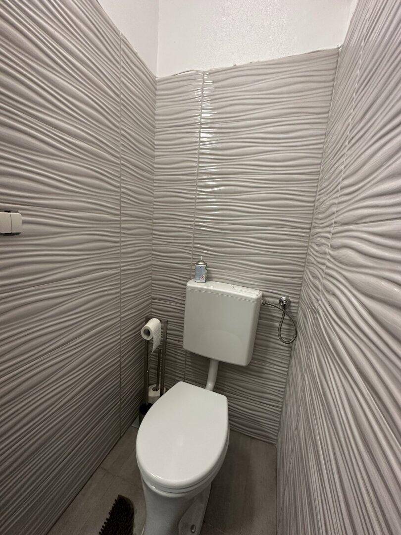 Separate Toilette mit modernen grauen Wandfliesen und Standard-WC.