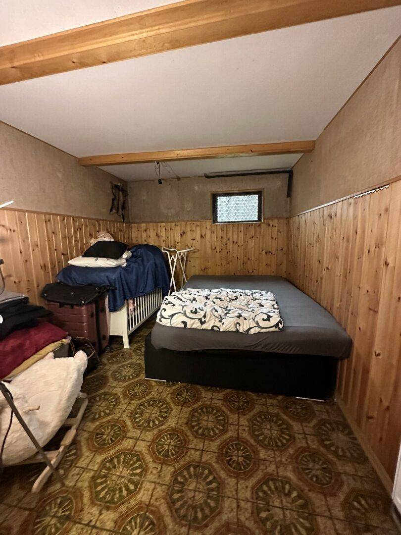 Schlafzimmer mit Holzvertäfelung an den Wänden, gemustertem Boden und sichtbaren Deckenbalken.