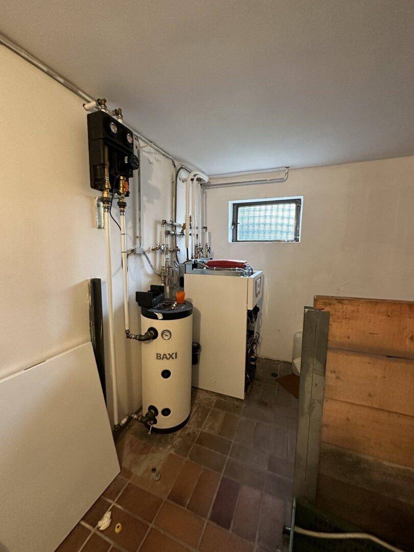 Heizungsraum im Keller mit Warmwasserspeicher und technischen Installationen.