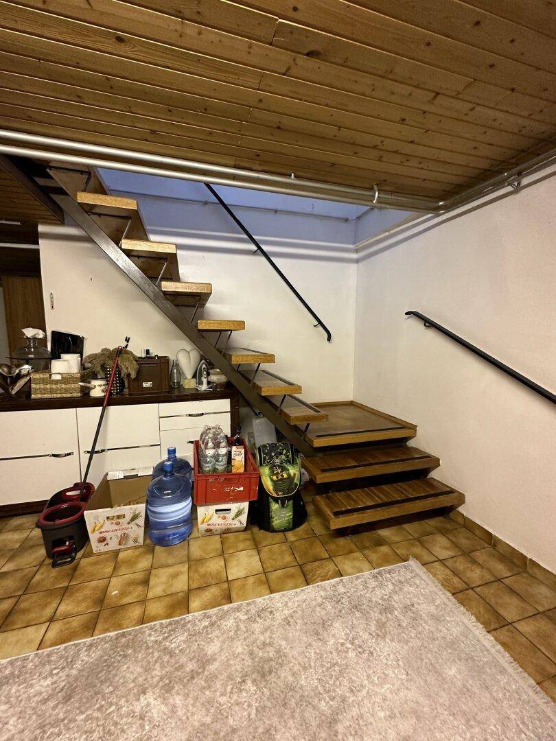 Holztreppe mit Metallgeländer in einem Bereich mit gefliestem Boden und Holzdecke.