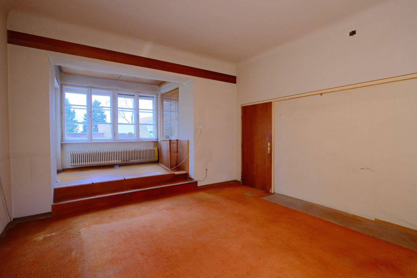 Wohnzimmer mit orangefarbenem Teppichboden und einem erhöhten Bereich mit Erkerfenster.