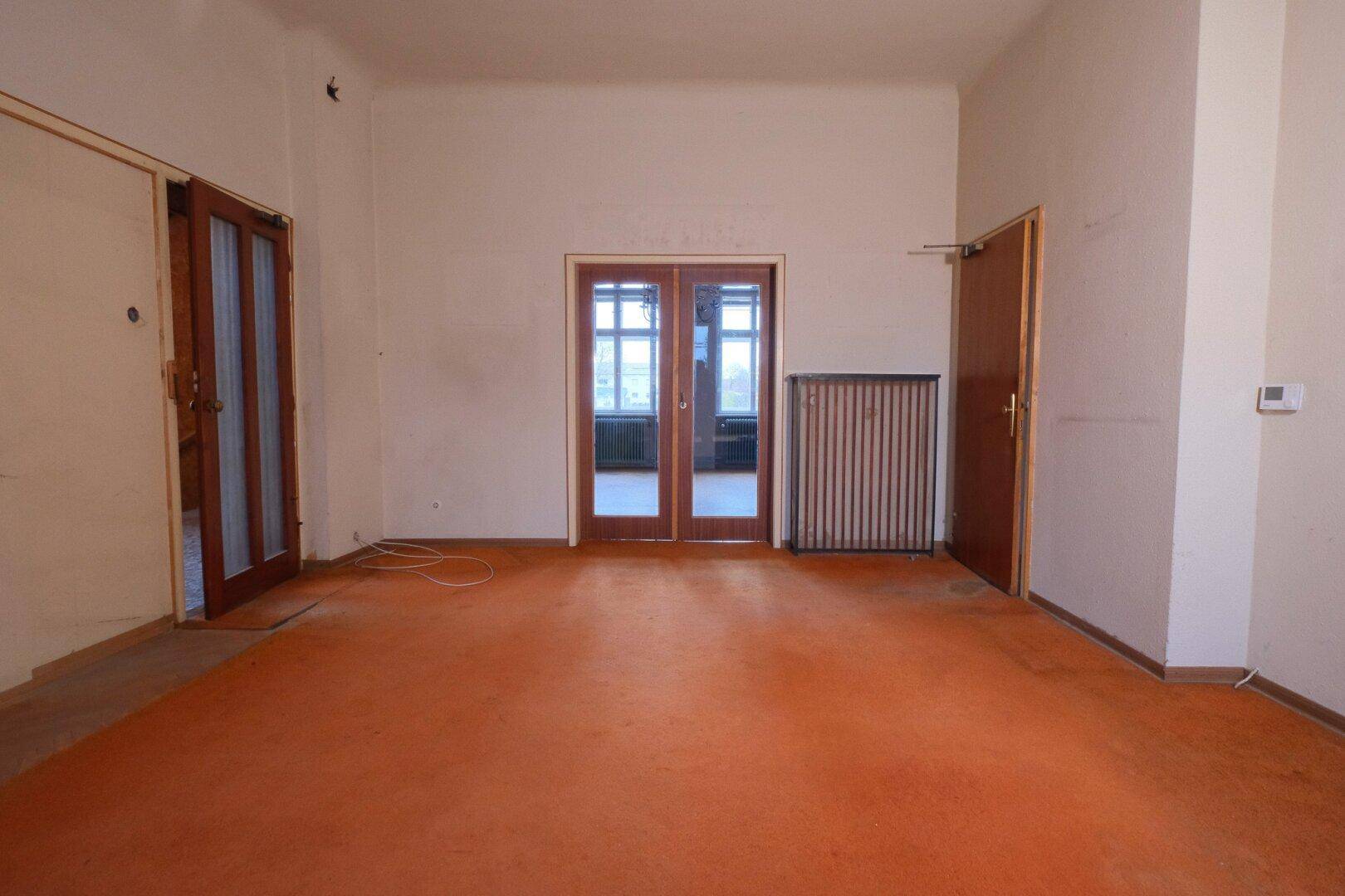 Geräumiges Wohnzimmer mit orangefarbenem Teppichboden und eleganten Holztüren.