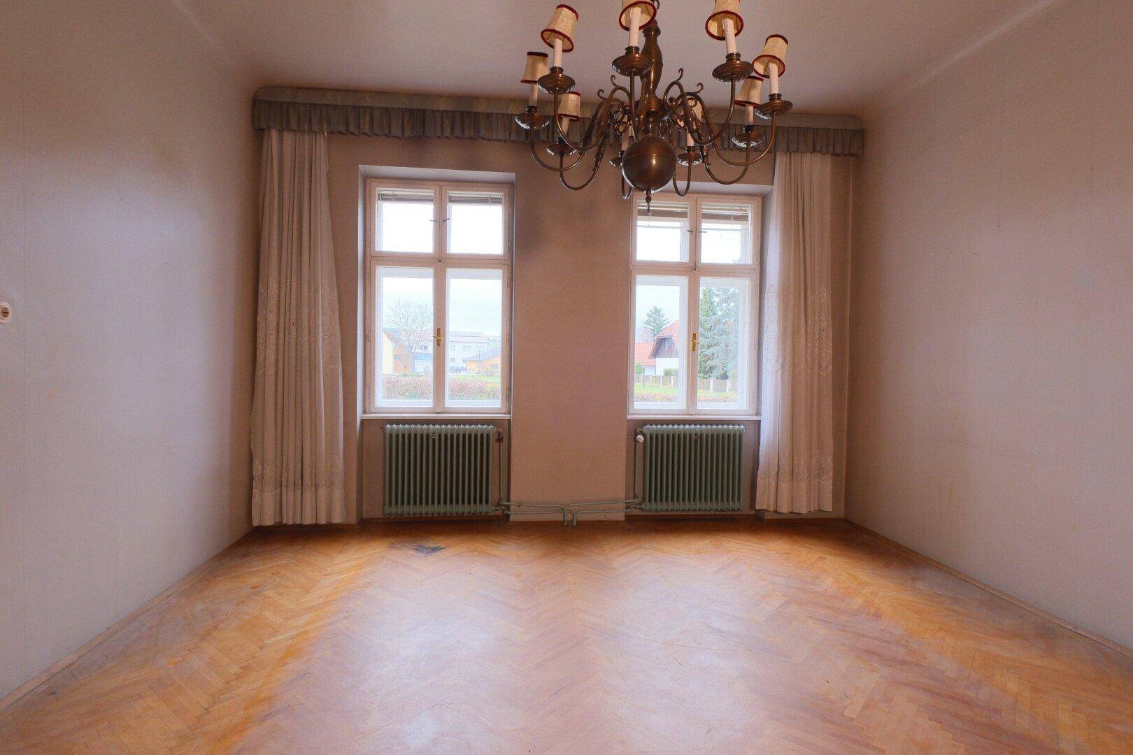 Helles Wohnzimmer mit Fischgrätparkett, hohen Fenstern und einem klassischen Kronleuchter.