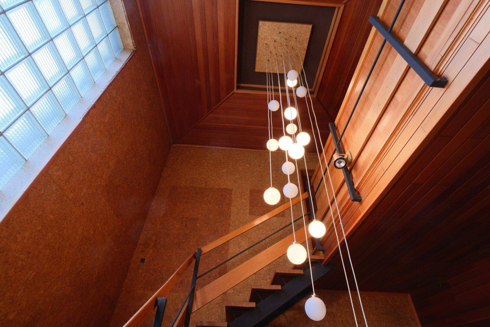 Treppenhaus mit Holzverkleidung, modernem Kronleuchter und Glasbausteinfenster.