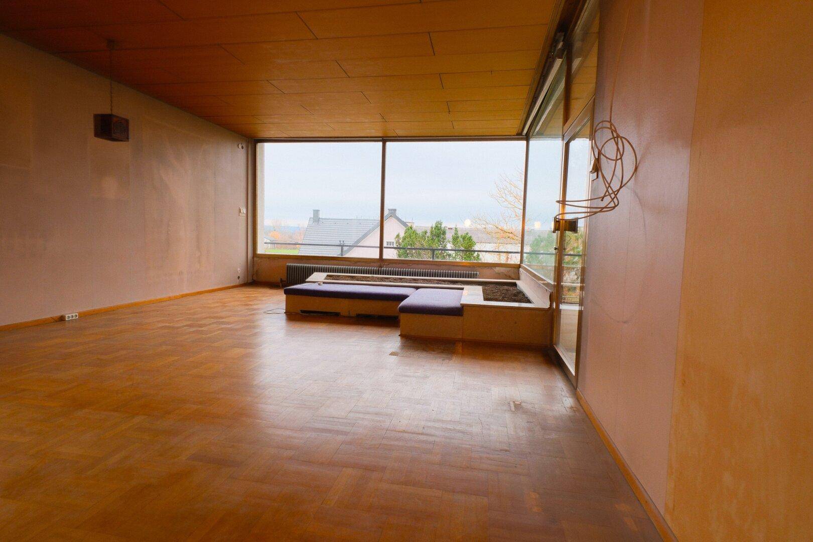 Großes Wohnzimmer mit Parkettboden, Panoramafenster und integrierten Sitzgelegenheiten.