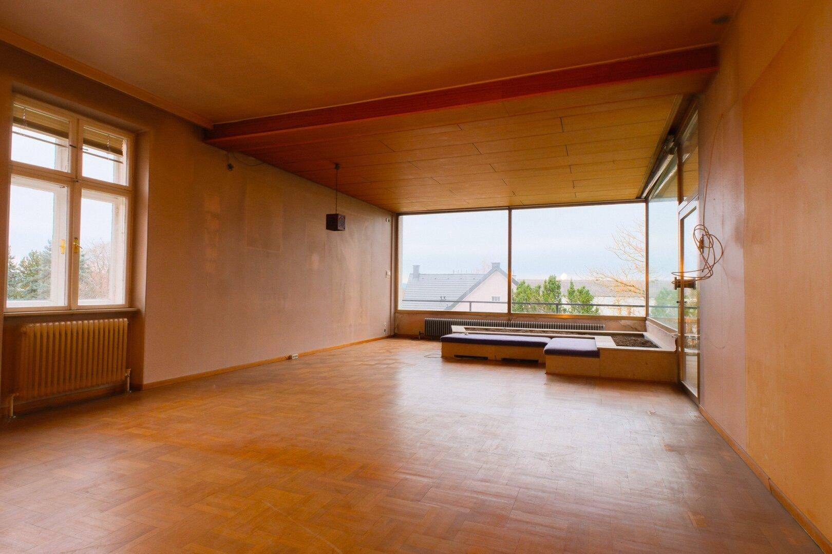 Geräumiges Wohnzimmer mit Parkettboden und einer beeindruckenden Fensterfront für viel Licht.