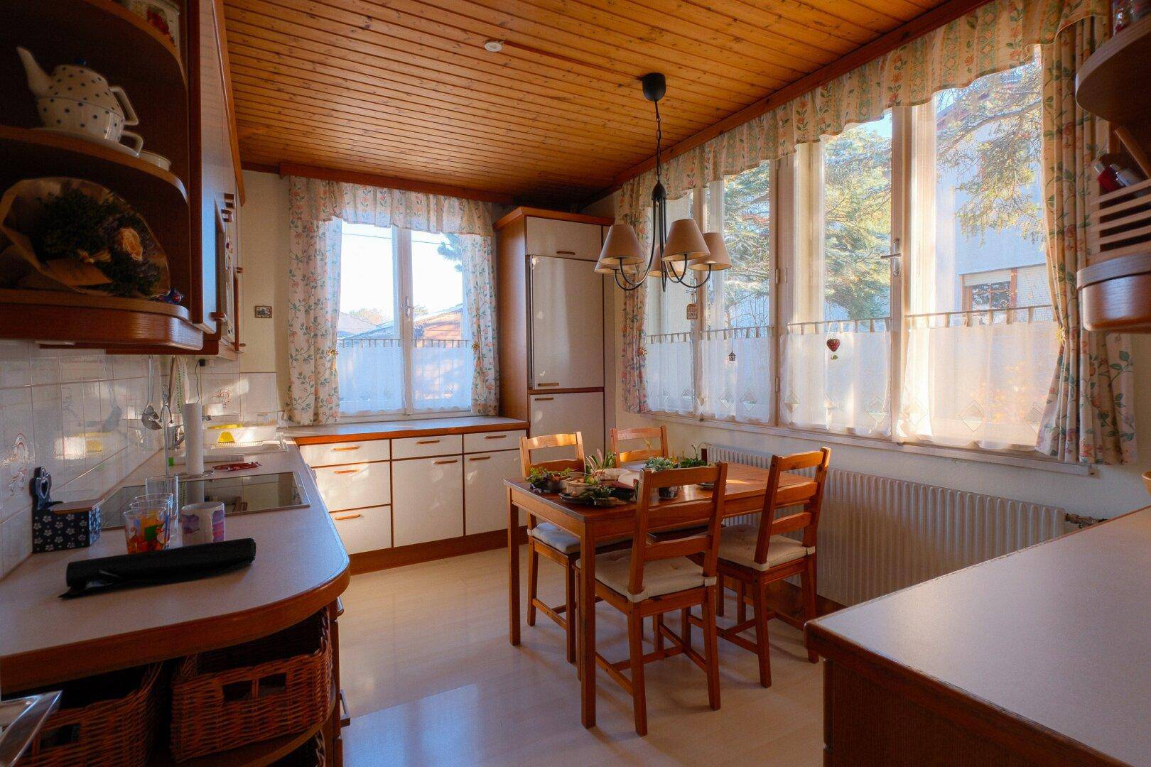 Gemütliche Wohnküche mit Holztäfelung, Essbereich und vielen Fenstern für natürliches Licht.