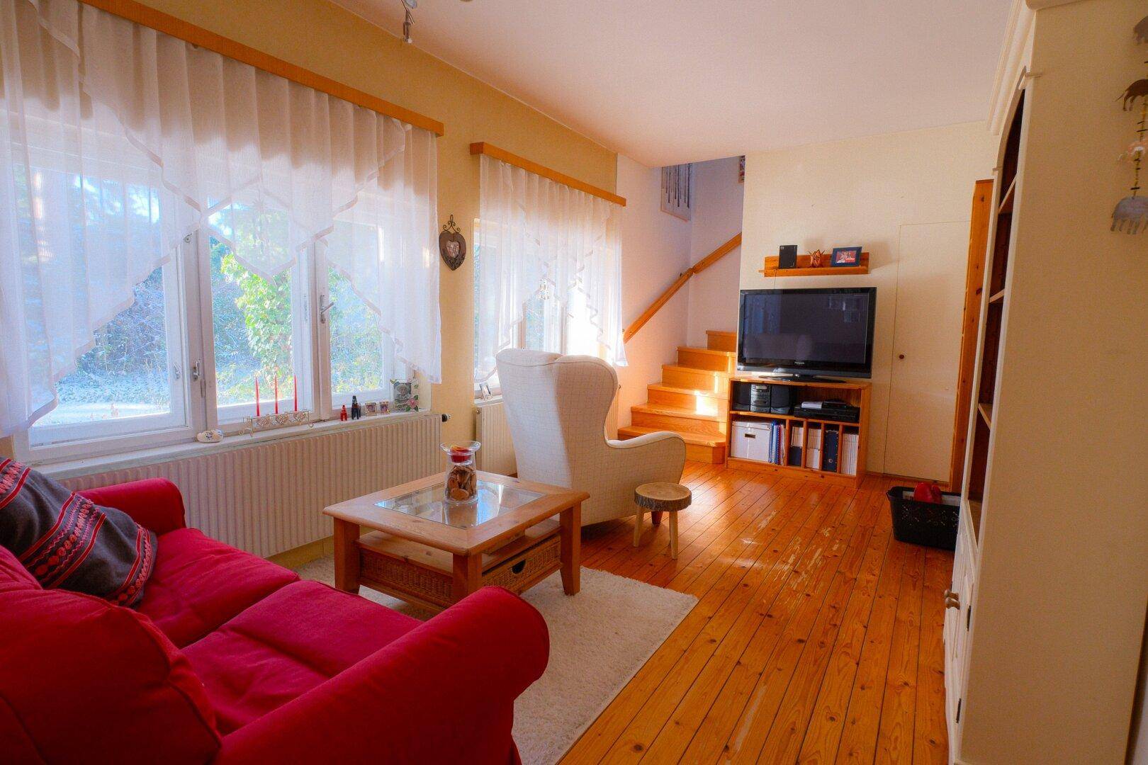 Helles Wohnzimmer mit Holzfußboden, rotem Sofa und Treppenzugang zum oberen Stockwerk.