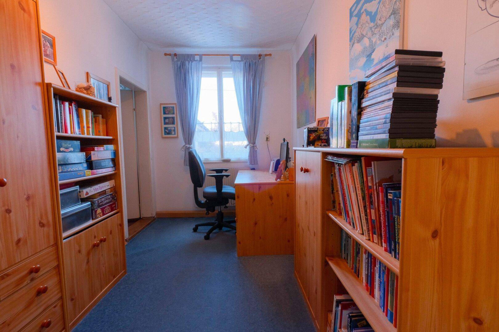 Arbeitszimmer mit Holzmöbeln, Teppichboden und einem Fenster, das viel Tageslicht hereinlässt.