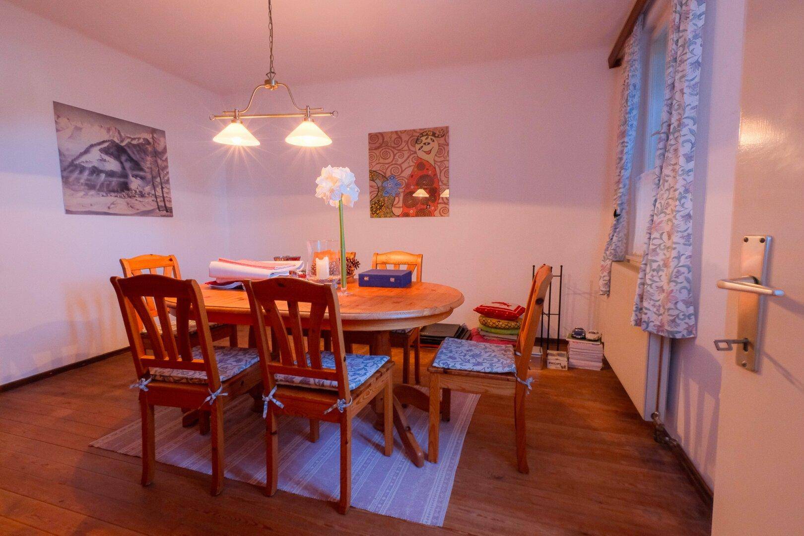Esszimmer mit Holztisch und Stühlen, Holzfußboden und dekorativen Bildern an den Wänden.