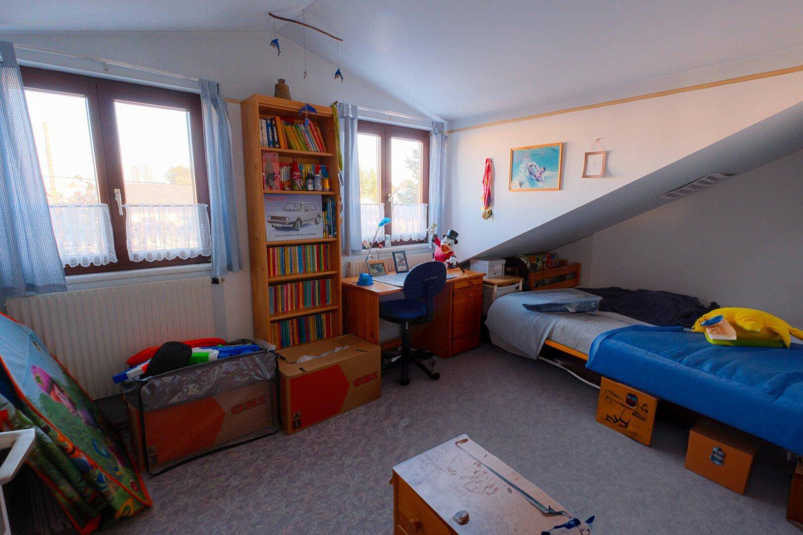 Kinderzimmer im Dachgeschoss mit Schrägen, Teppichboden und zwei Fenstern für viel Licht.