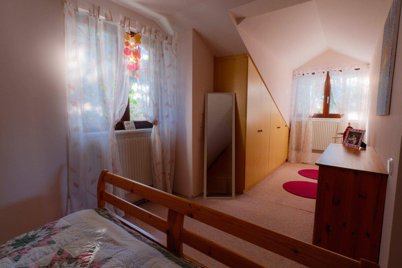 Schlafzimmer im Dachgeschoss mit Schrägen, Teppichboden und Einbauschränken für Stauraum.
