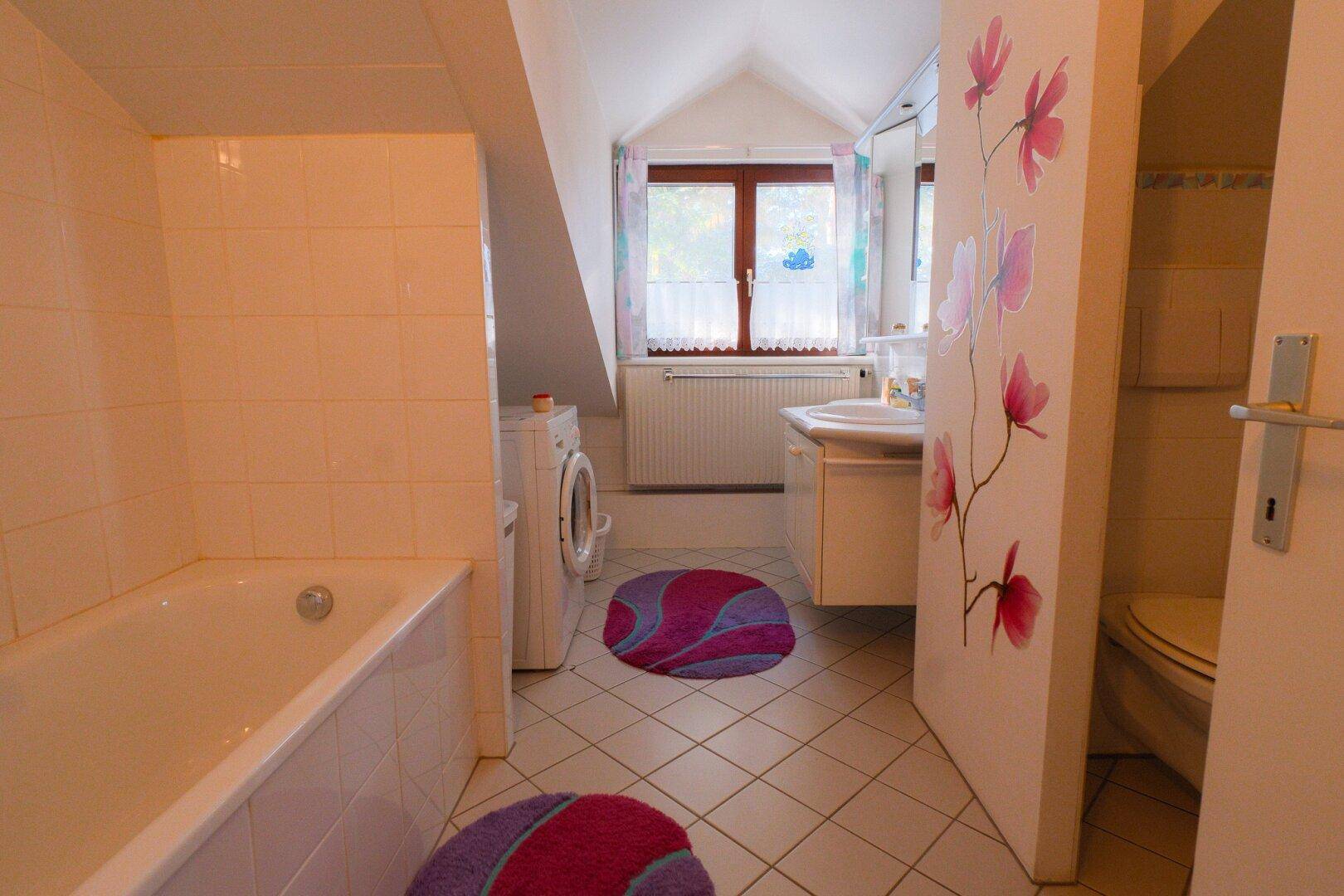 Badezimmer im Dachgeschoss mit Badewanne, Waschmaschine und Fenster für natürliche Belüftung.