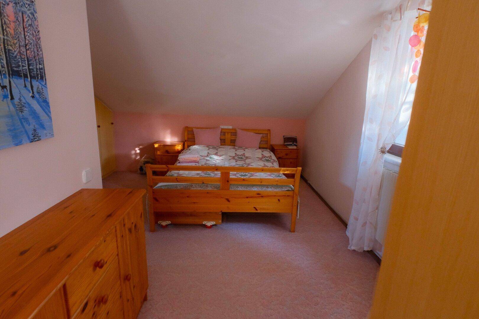 Geräumiges Schlafzimmer im Dachgeschoss mit Doppelbett, Holzmöbeln und Teppichboden.