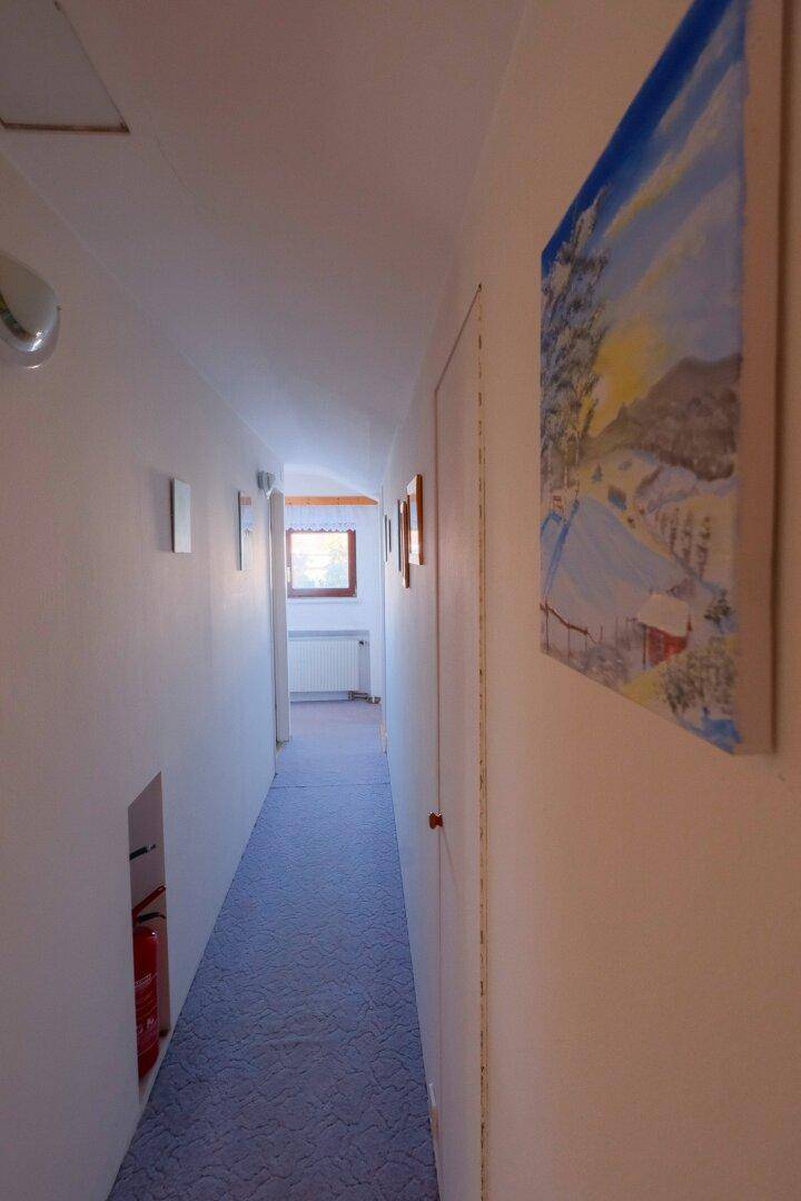 Langer Flur im Obergeschoss mit Teppichboden und einem Fenster am Ende, das Licht spendet.