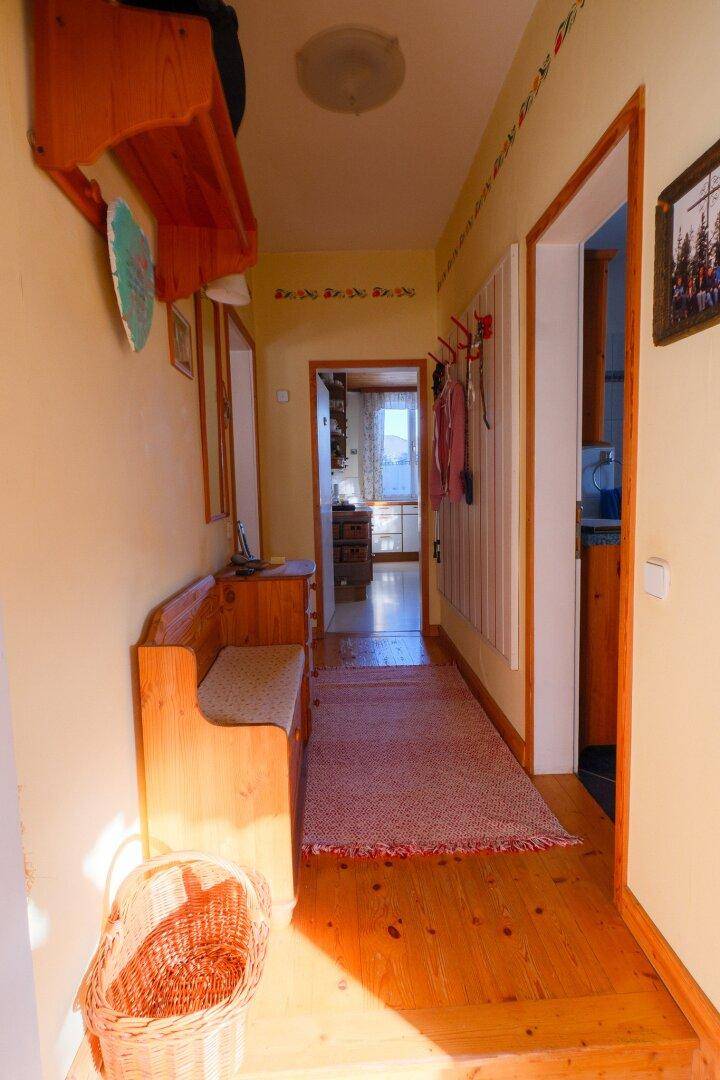 Eingangsbereich mit Holzbank, Garderobe und Blick in die angrenzende Küche.