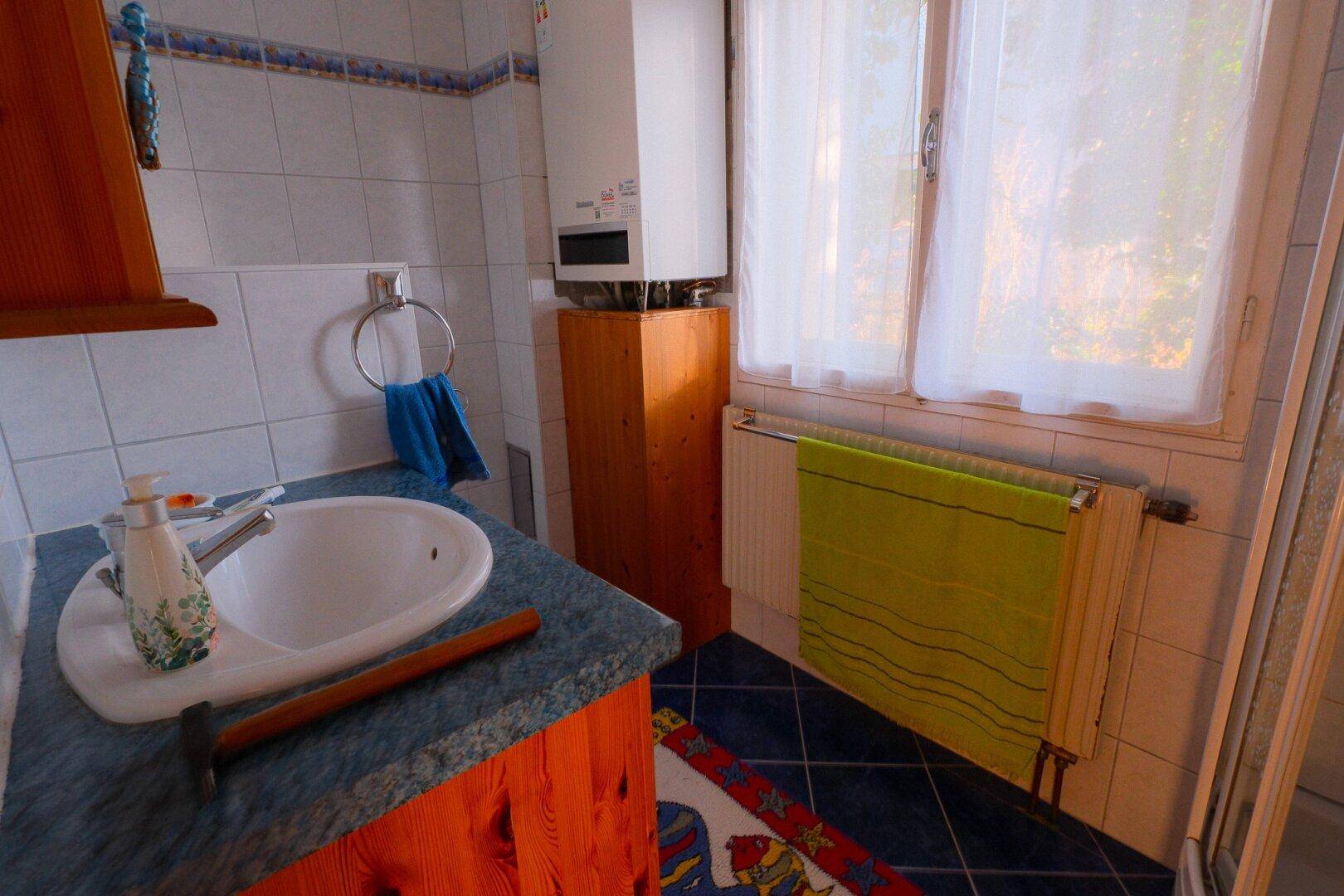 Funktionales Badezimmer mit blauen und weißen Fliesen, Waschbecken, Boiler und Fenster für Tageslicht.