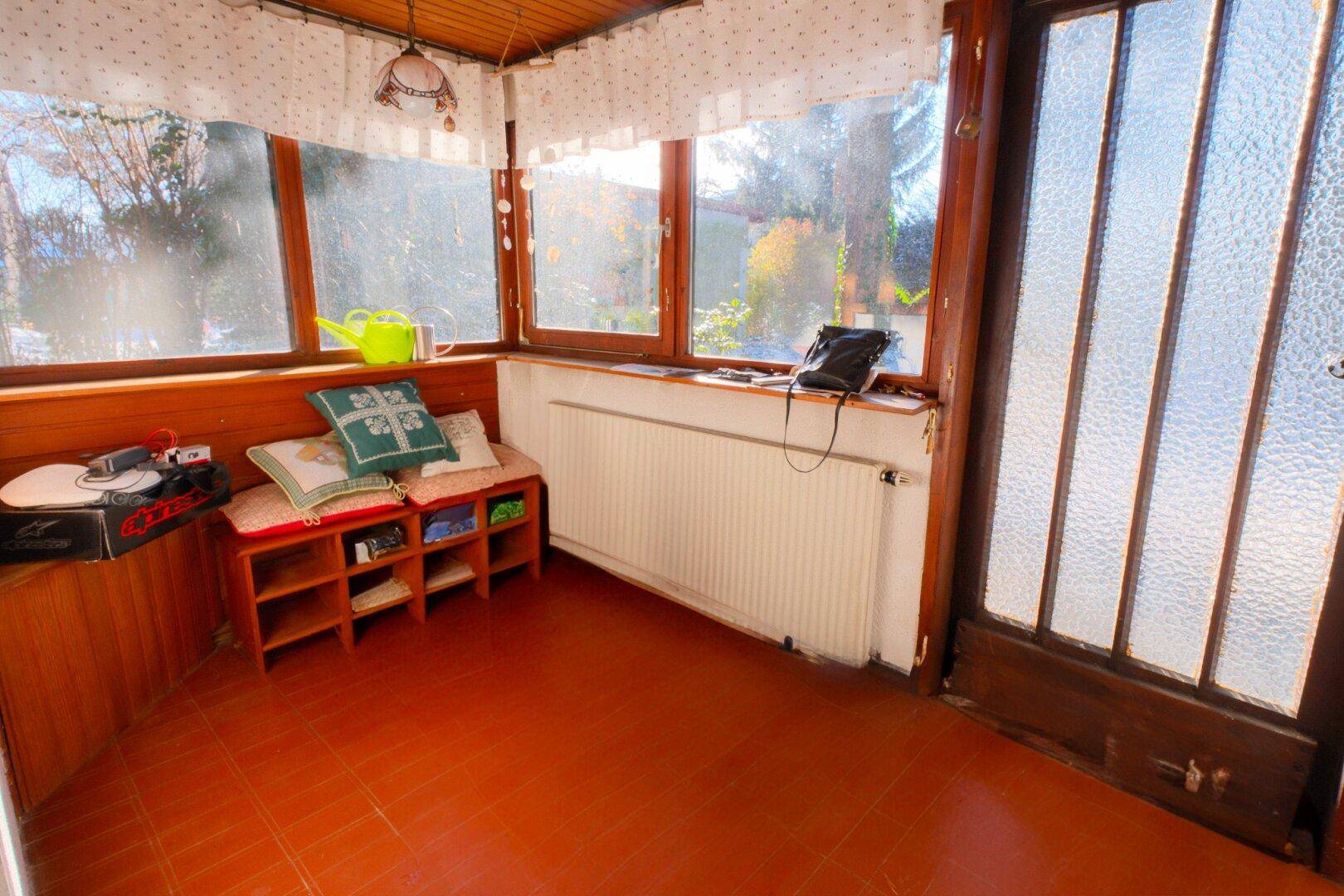 Gemütlicher Wintergarten mit großen Fenstern, Terrakotta-Bodenfliesen und einer integrierten Sitzbank.