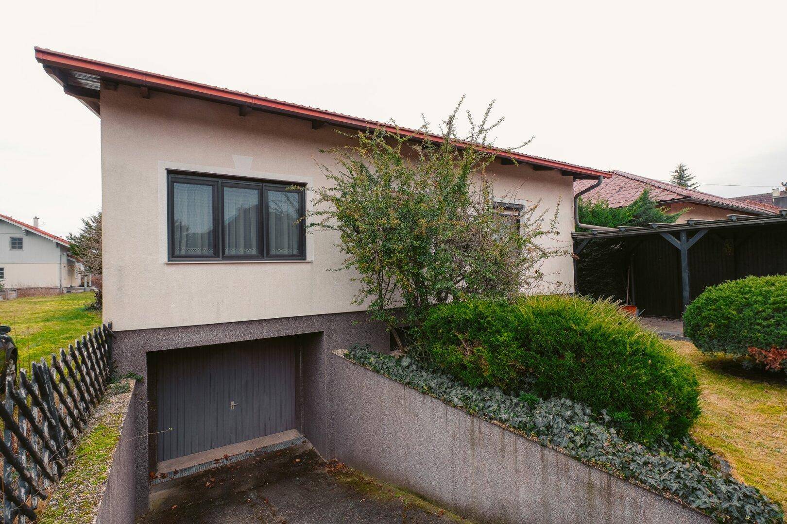 Hausfassade mit integrierter Tiefgarage und gepflegter Bepflanzung am Hang.