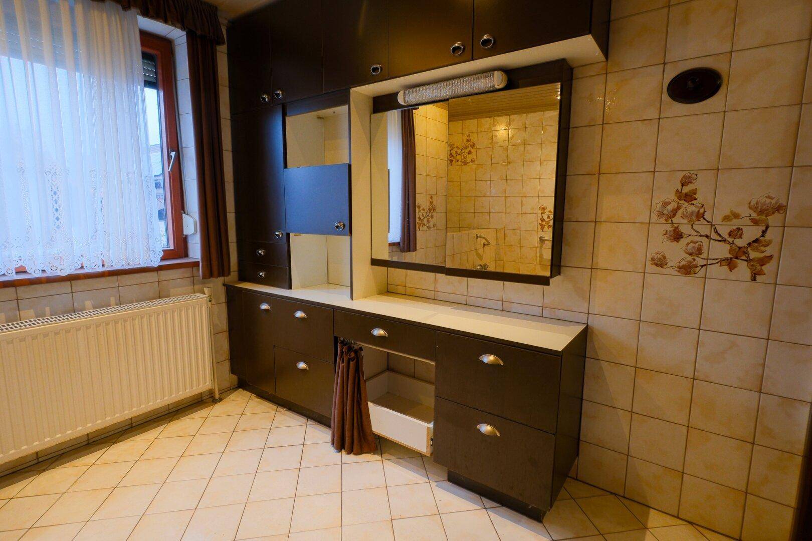 Badezimmer mit großem Waschtischunterschrank, Spiegel und passenden Fliesen.