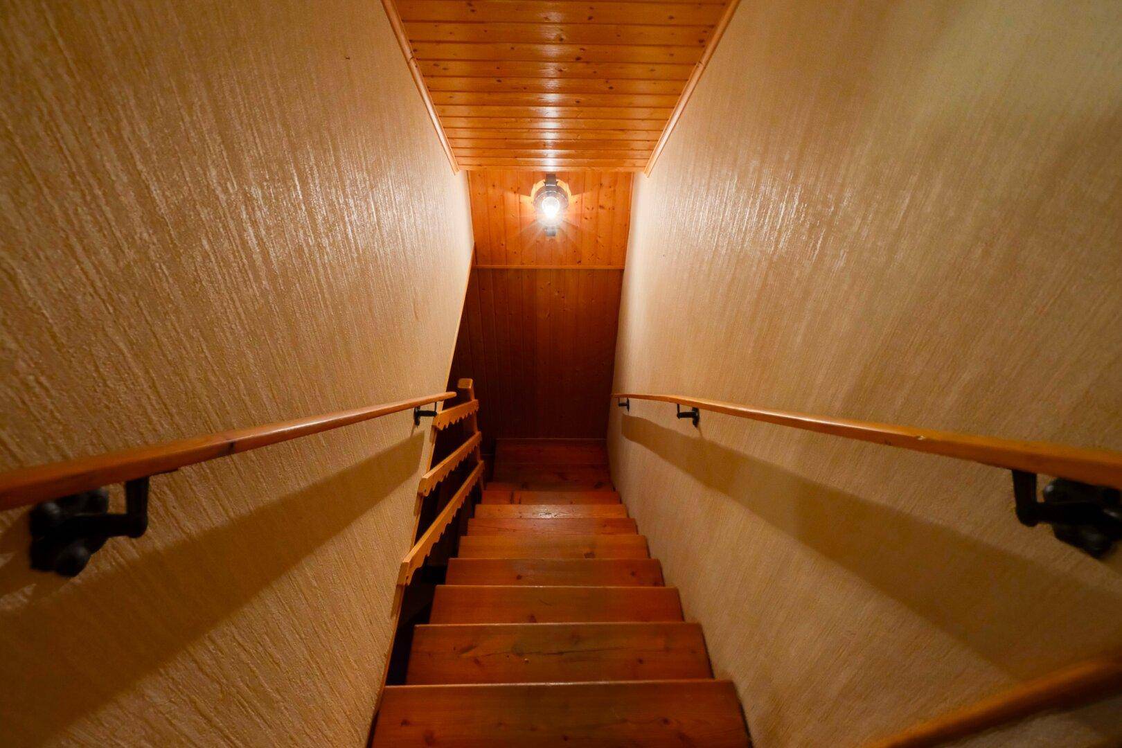 Holztreppe mit Handläufen führt in den Kellerbereich mit Holzdecke.