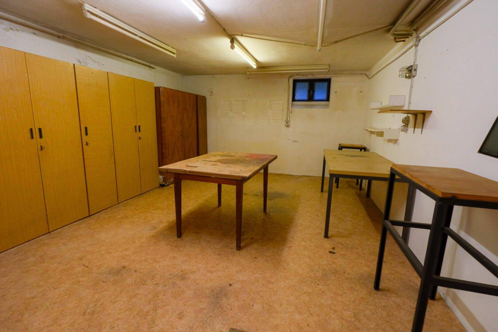 Geräumiger Kellerraum mit Schränken, Tischen und Linoleumboden.