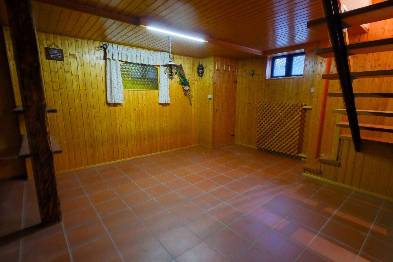 Ausgebauter Kellerraum mit Holzvertäfelung, Fliesenboden und kleinem Fenster.