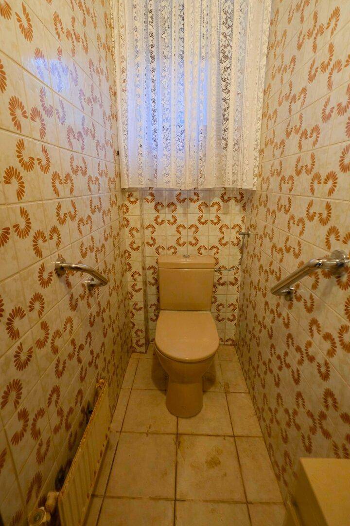 Gäste-WC mit gemusterten Fliesen, beiger Toilette und Fenster.