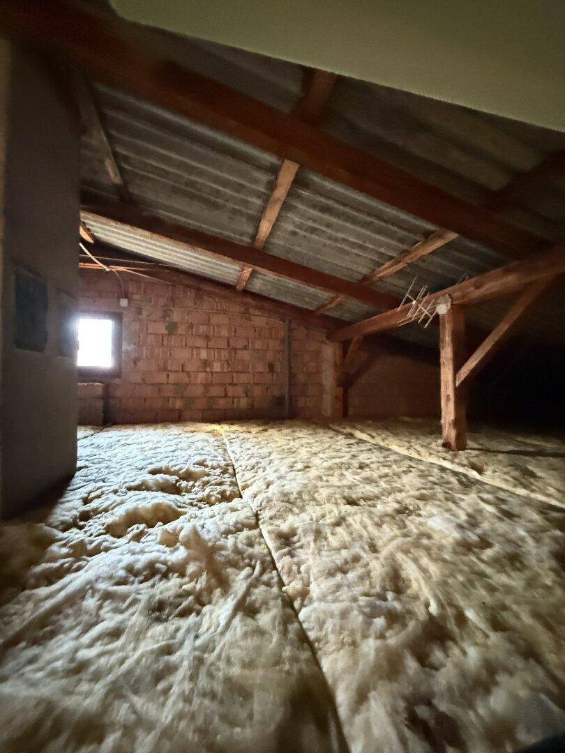 Dachboden mit Ziegelwänden, Holzbalken und kleinem Fenster.