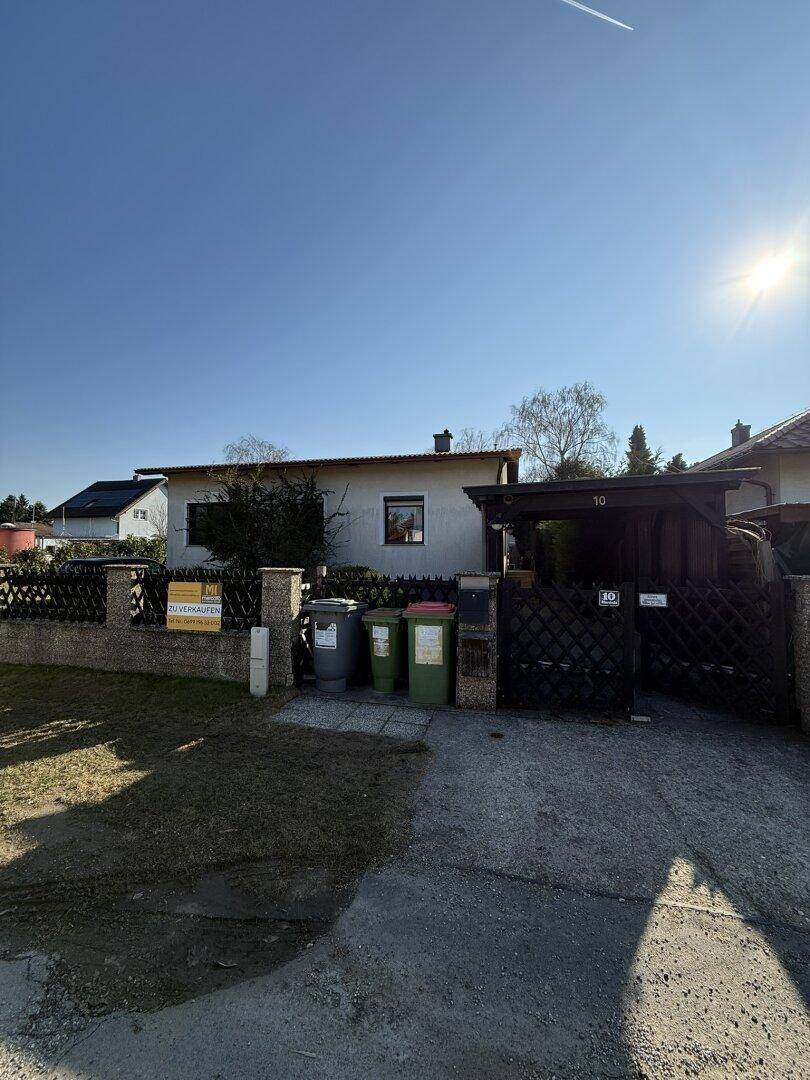 Vorderansicht des Hauses mit Zaun, Mülltonnen und Carport an der Straße.