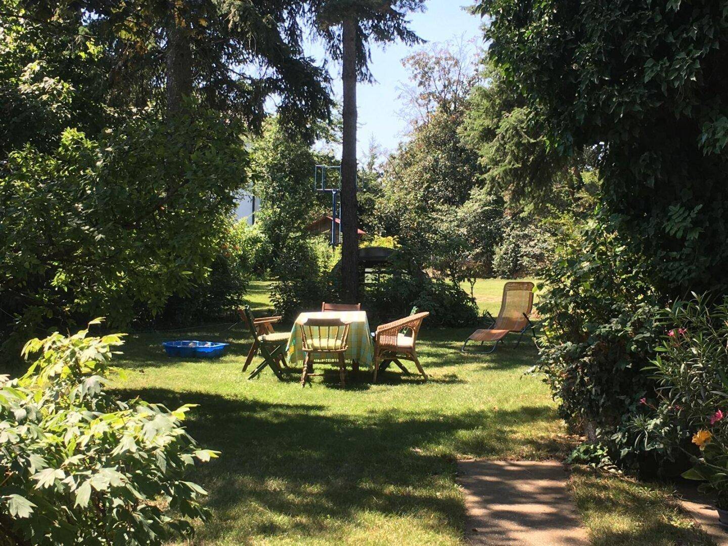 Großer, gepflegter Garten mit Sitzbereich unter Bäumen und viel Grünfläche zum Entspannen.