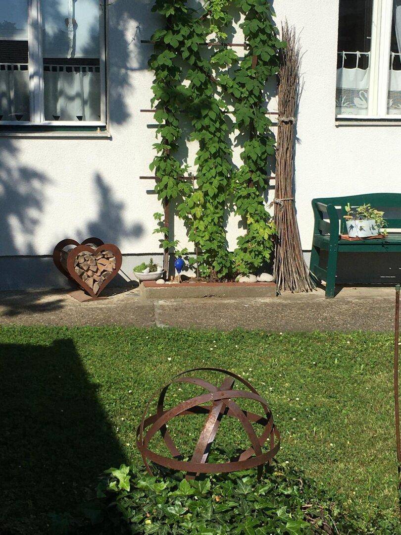 Detailansicht der Hausfassade mit Kletterpflanzen, einer Gartenbank und dekorativen Elementen im Garten.