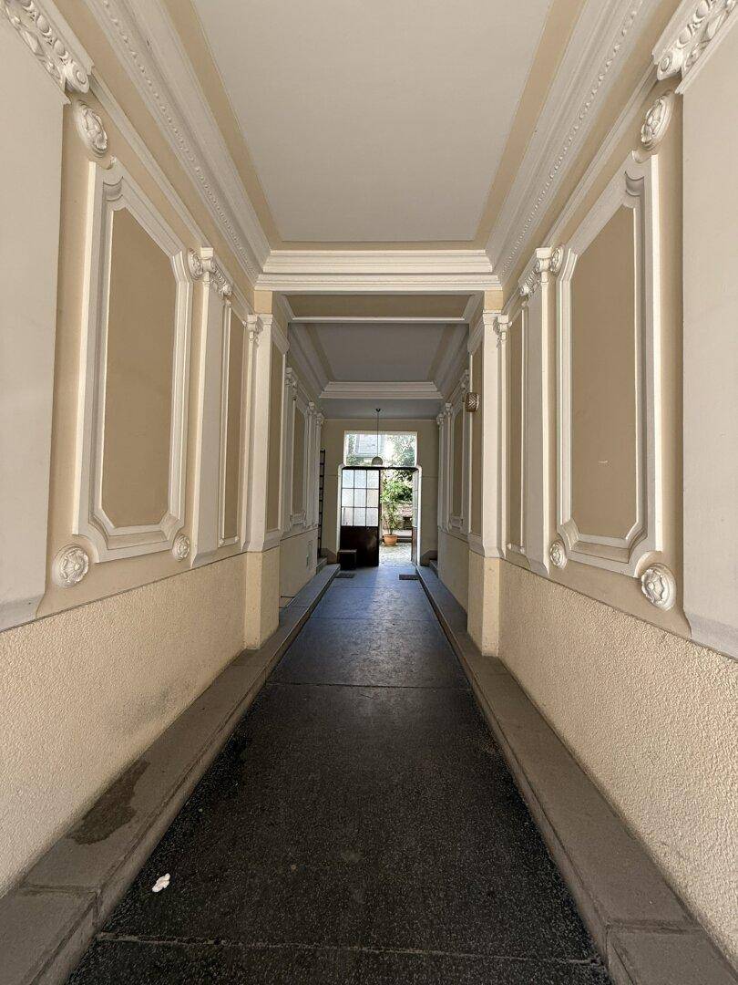 Langer, historischer Eingangsbereich mit Stuckverzierungen und Blick ins Grüne am Ende.