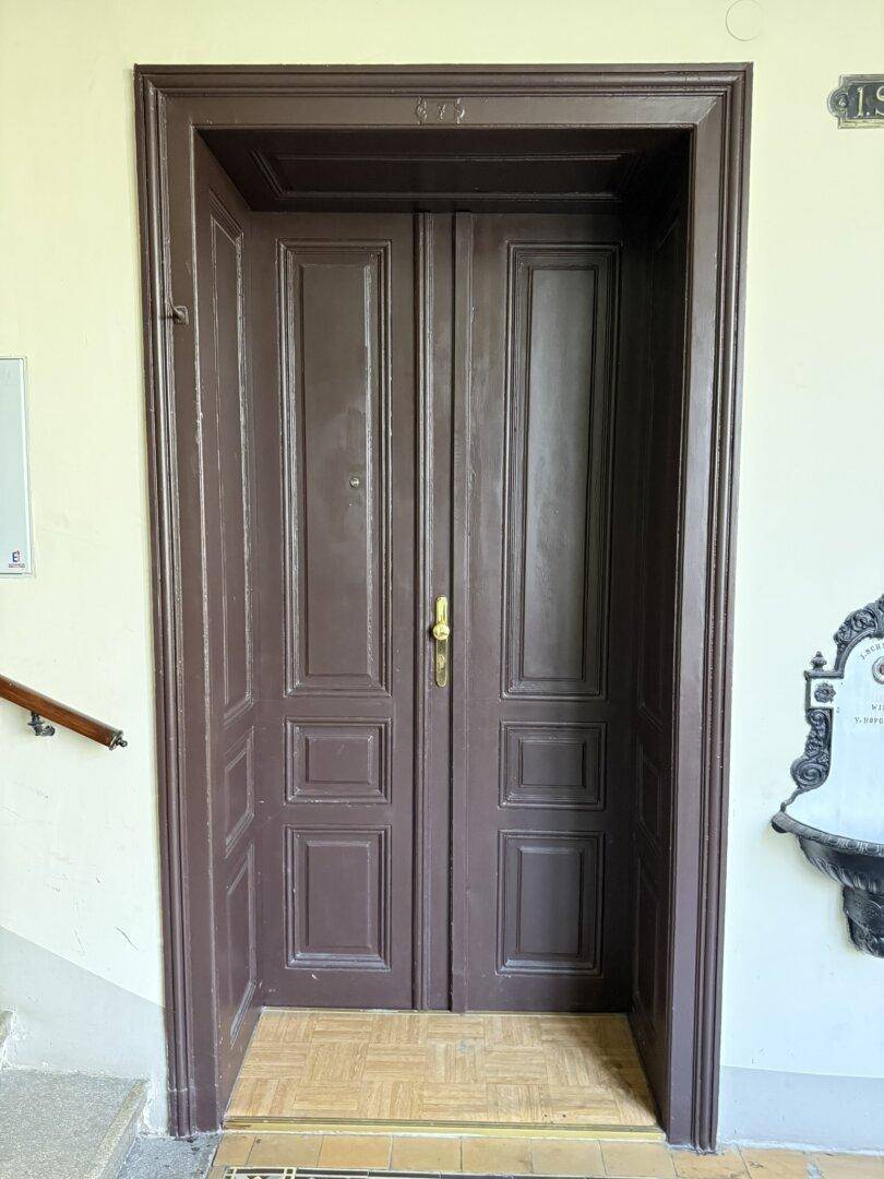 Massive, verzierte Holztür mit goldenem Griff, die den Eingang zur Wohnung markiert.